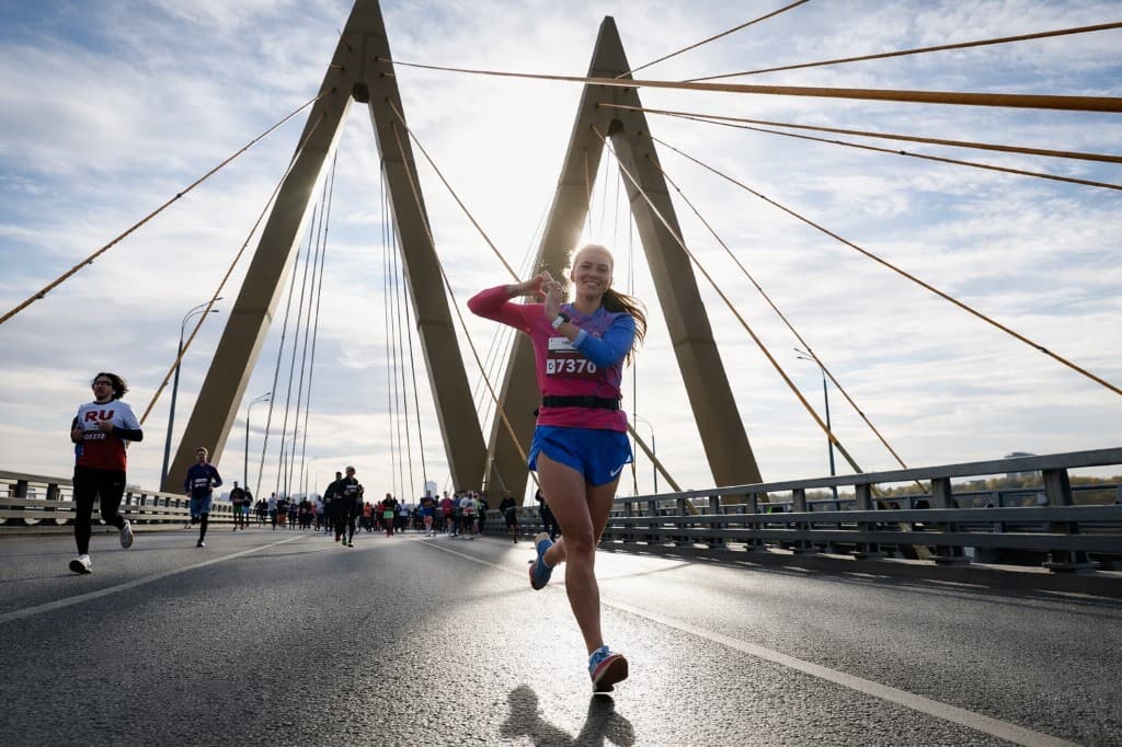 Участница забега бежит по вантовому мосту навстречу солнцу — улыбка, движение, свет сквозь тросы.