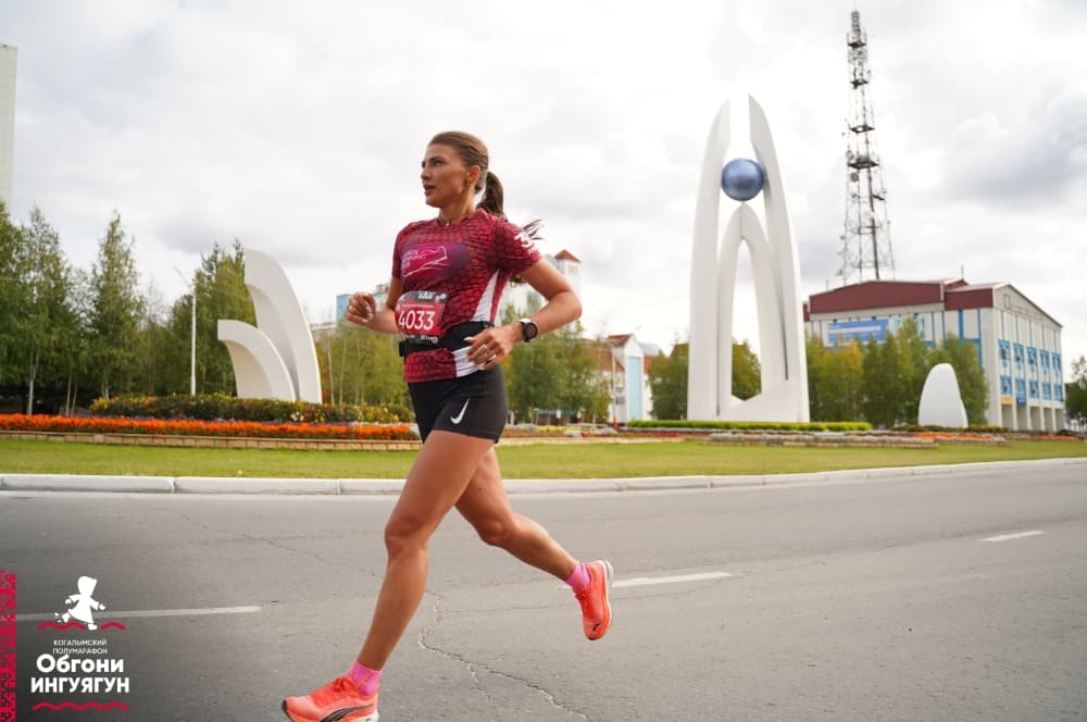Участница полумарафона в беговой форме на фоне городского монумента.